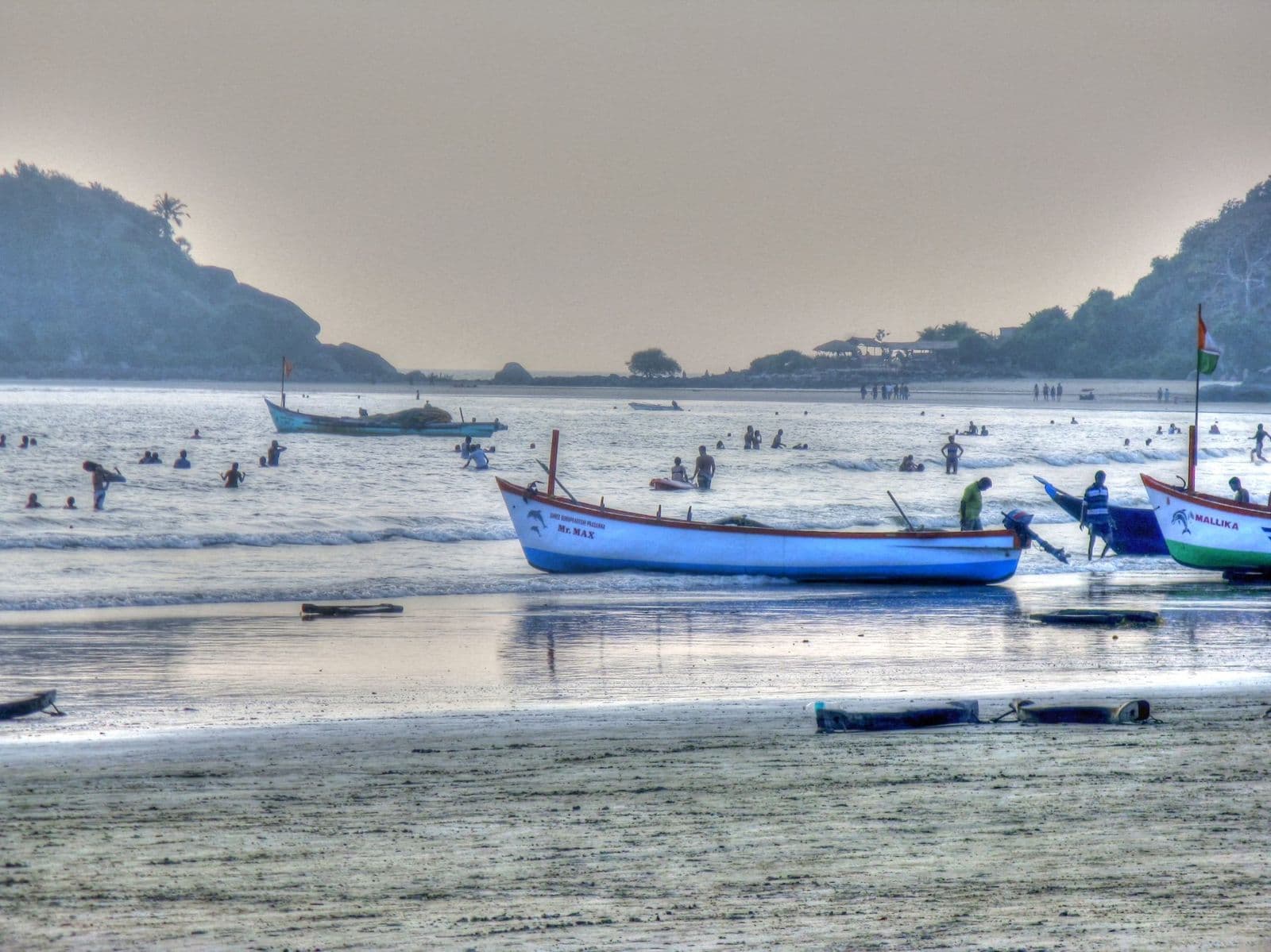 Fishing boats pulled up on the shallows of Palolem beach, with a wooded headland behind