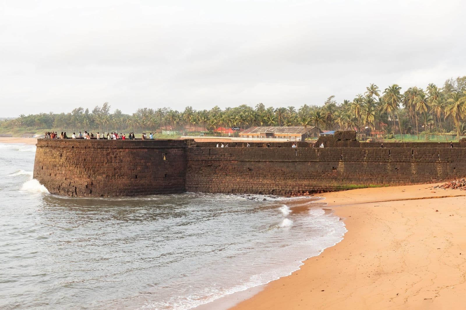 The laterite walls of Lower Aguada Fort meeting the sea beside a sandy beach