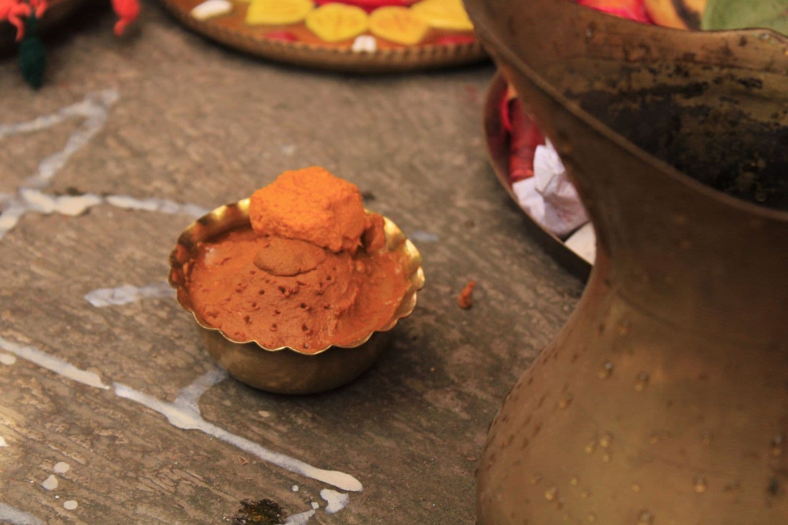 A small brass bowl heaped with raw turmeric paste beside a brass vessel, ready for a haldi ceremony
