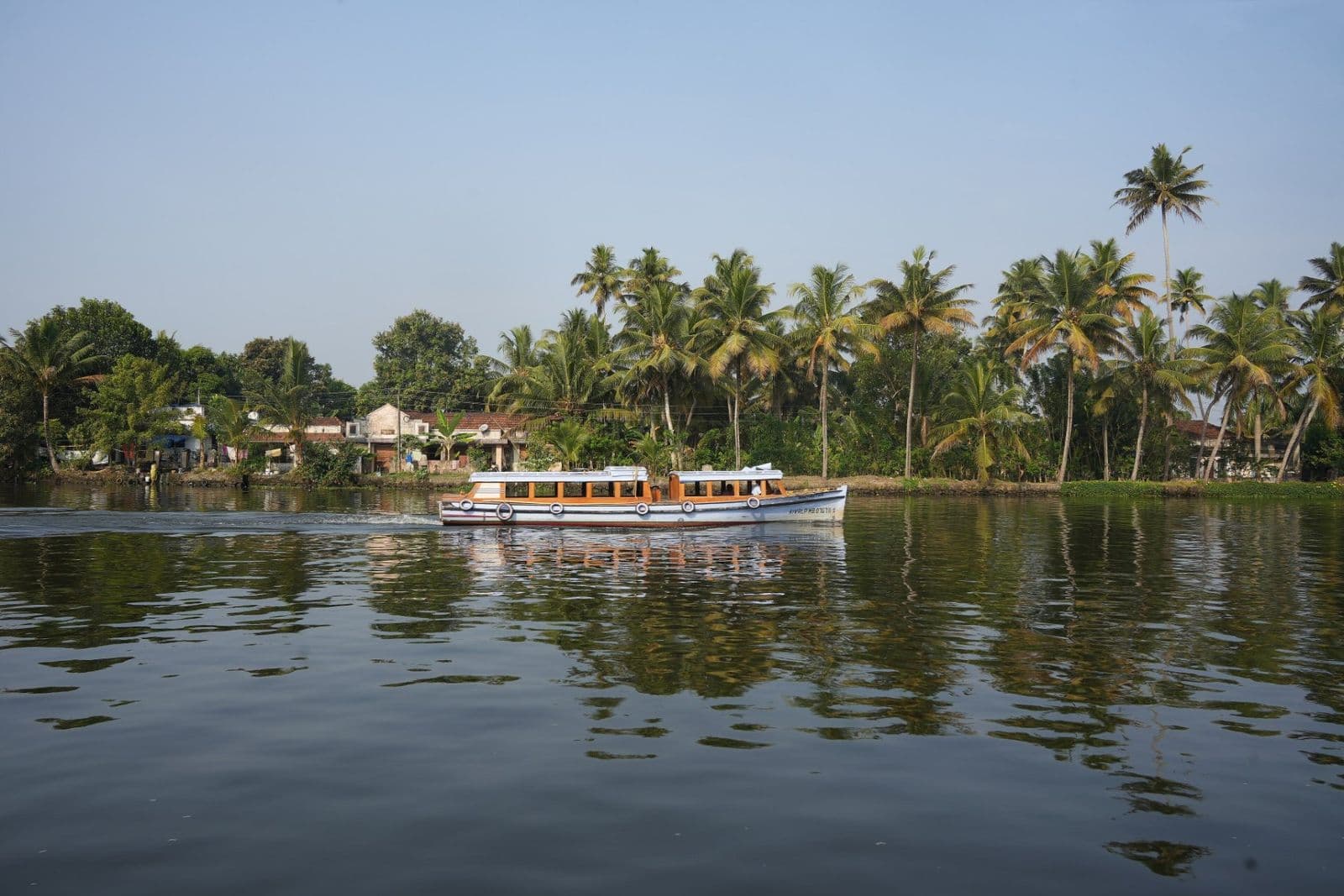 A wide stretch of backwater with a passing ferry and a line of palms on the far bank