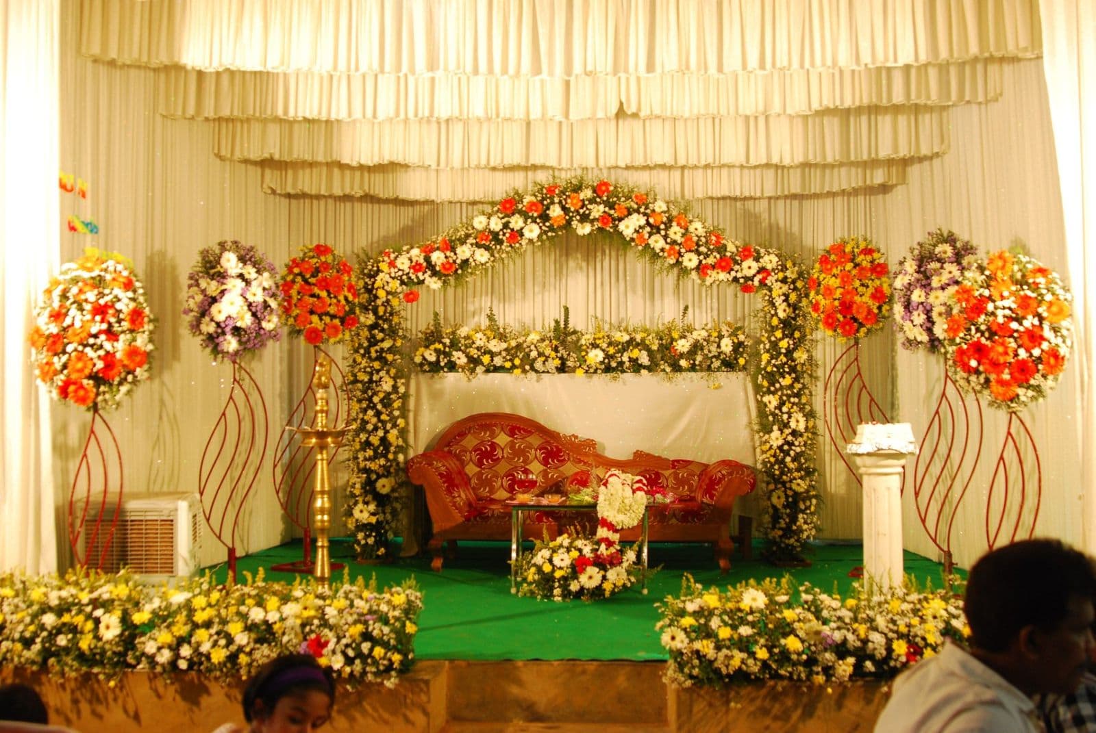 A wedding stage dressed with white drapes, flower arches and a red sofa for the couple