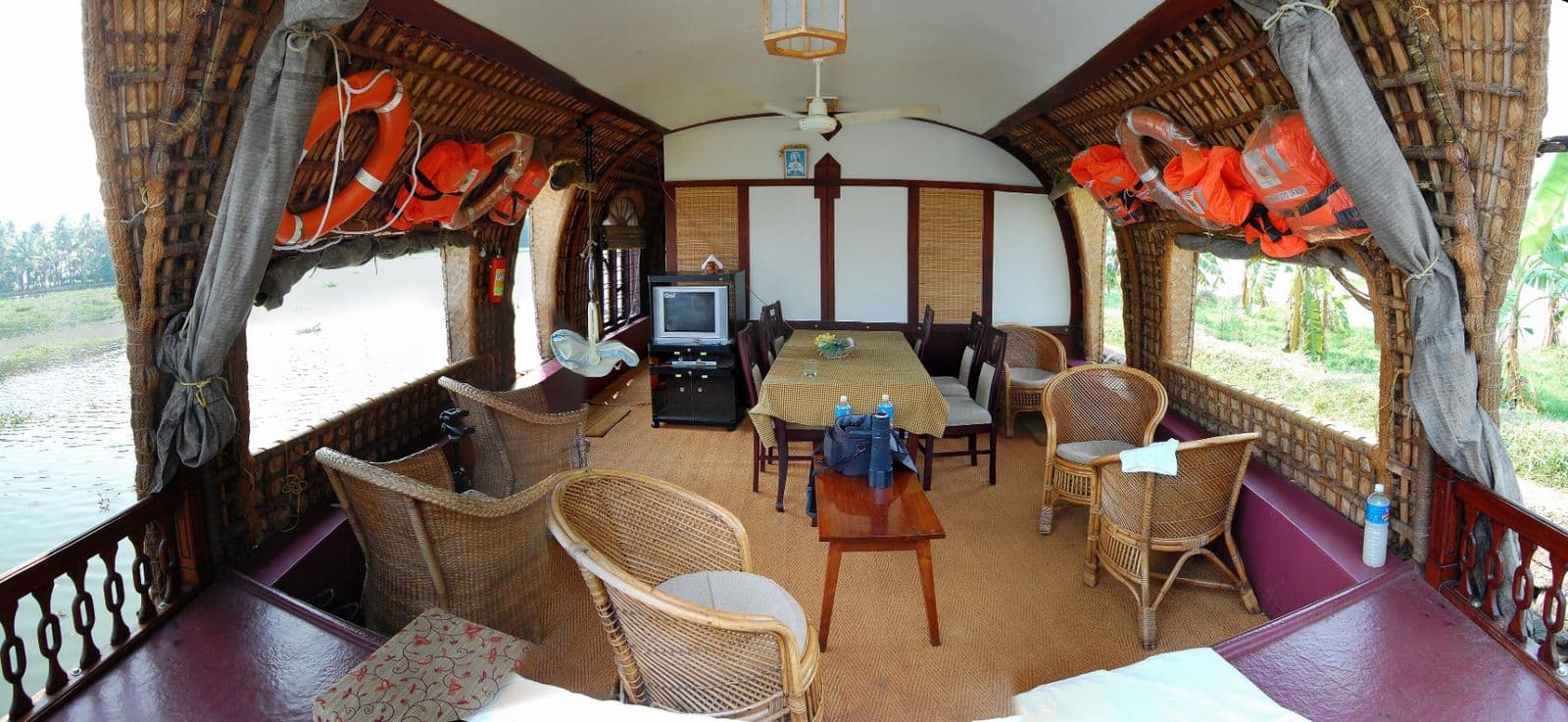 The lounge inside a kettuvallam houseboat, with cane chairs, a dining table and windows on both sides