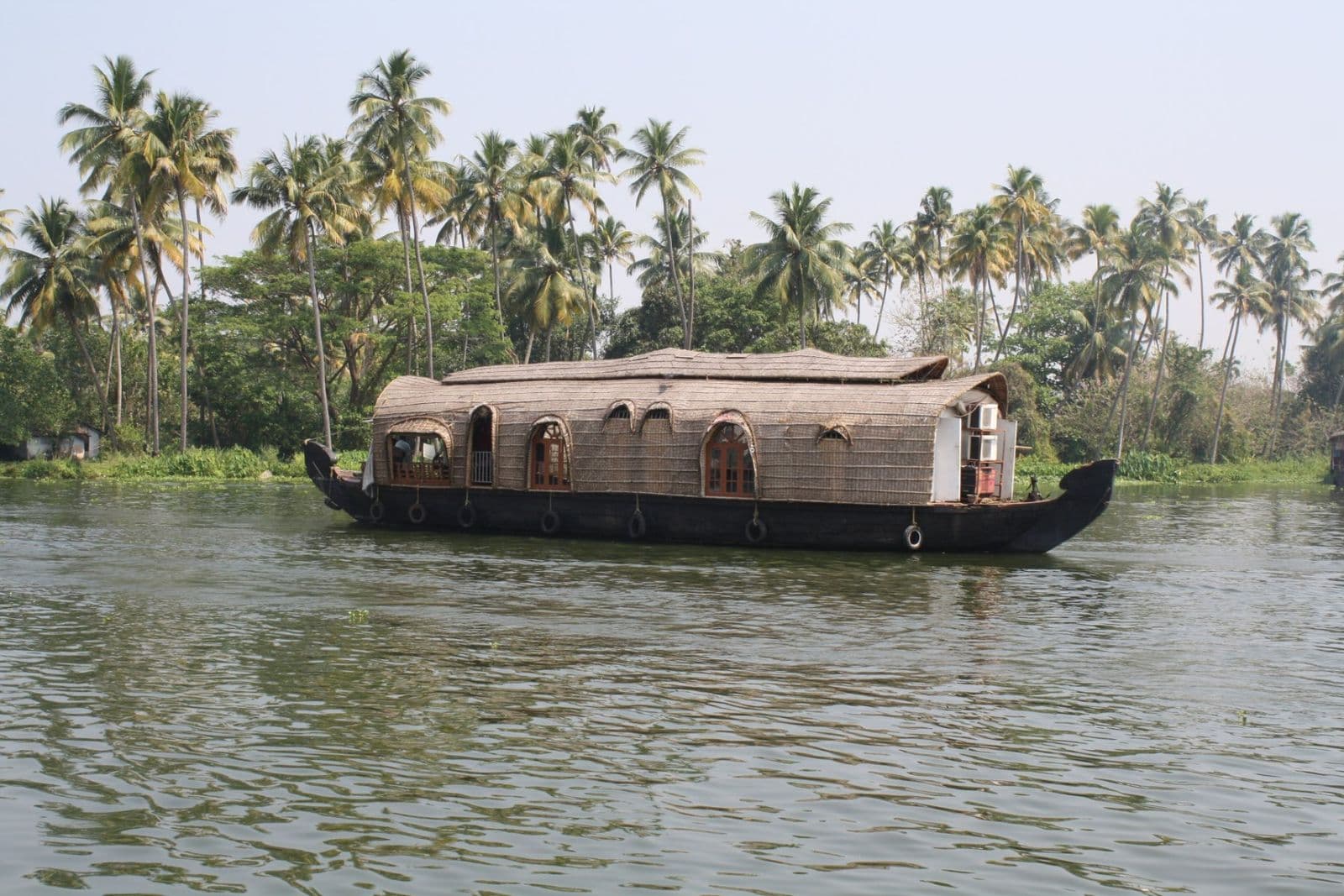 A kettuvallam houseboat on Vembanad Lake with coconut palms along the shore