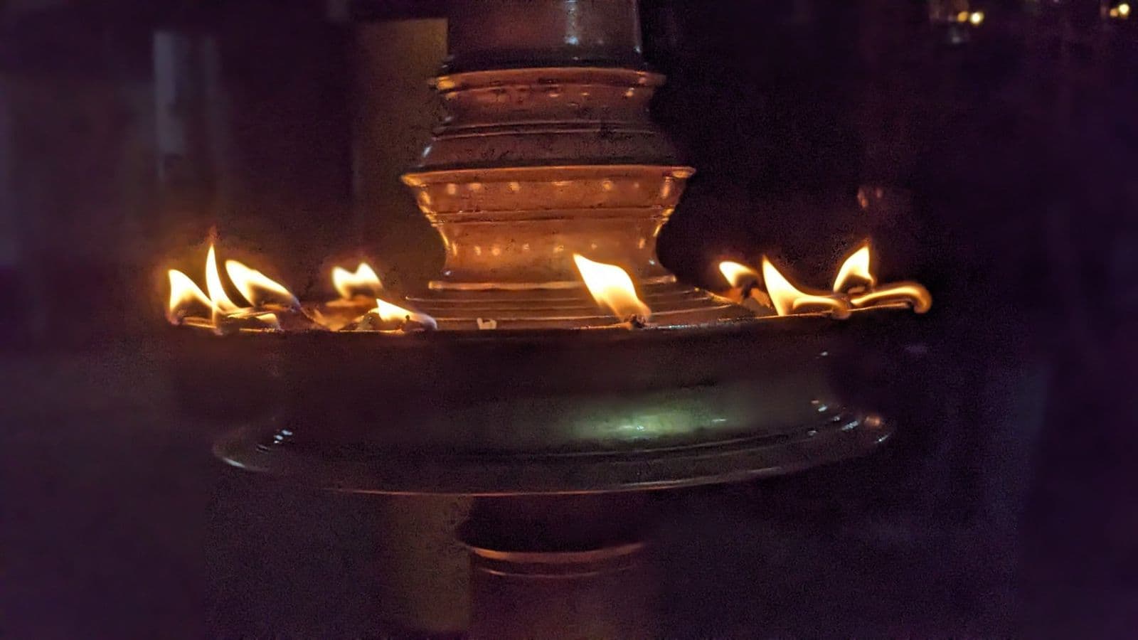 A brass nilavilakku oil lamp with its wicks lit in a dark temple