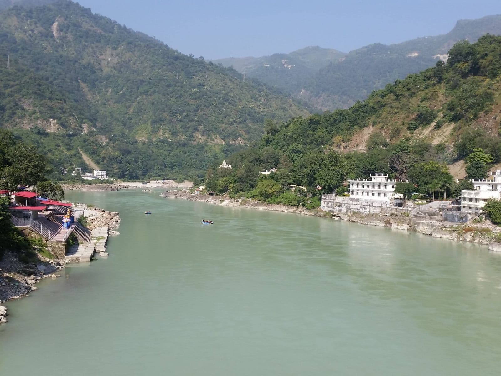 The green Ganges flowing through a steep, forested valley at Rishikesh