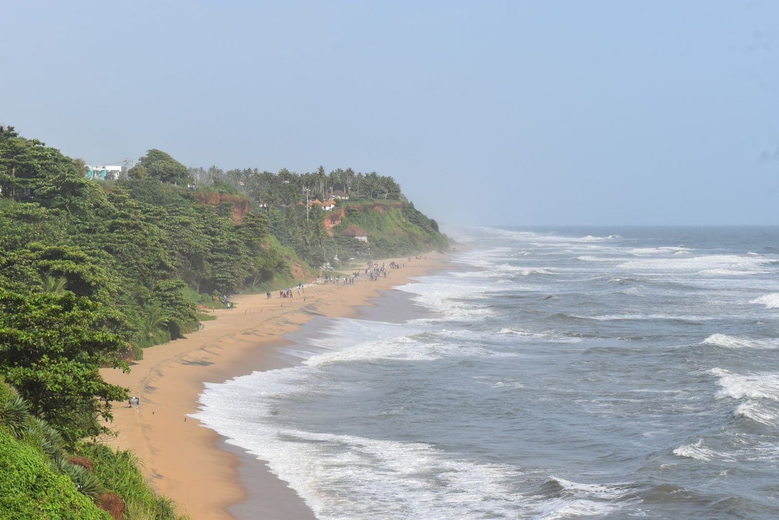 The green clifftop at Varkala above a long beach with rolling waves